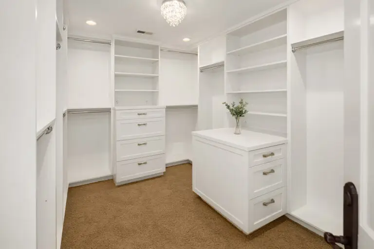 Walk-in closet with crystal chandelier, white shelving and center island dresser