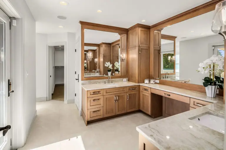 Cherry wood vanities with Taj Mahal quartzite counters, framed mirrors and doorway to the walk-in closet