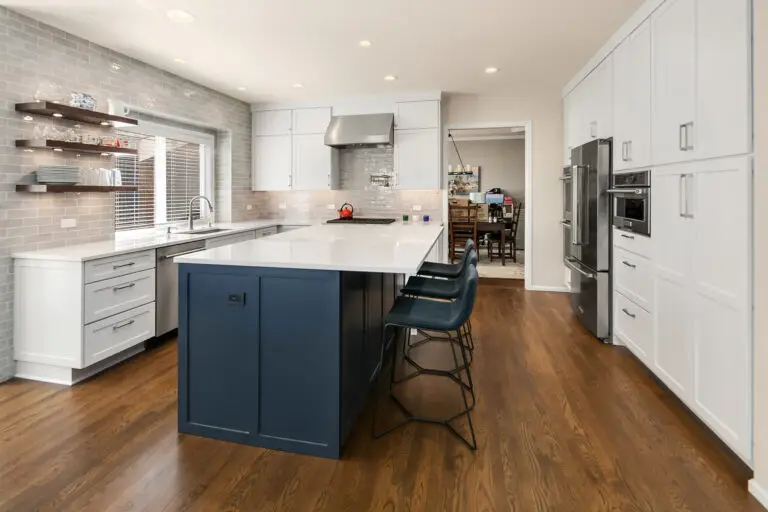 Remodeled kitchen with navy blue island, white quartz countertops, gray subway tile backsplash, and oak floors