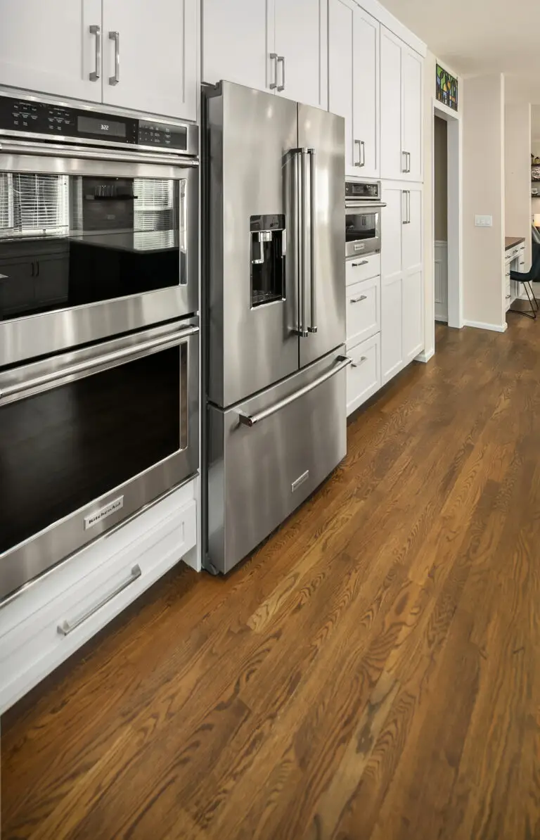 Stainless double oven and French-door refrigerator built into floor-to-ceiling white shaker cabinets