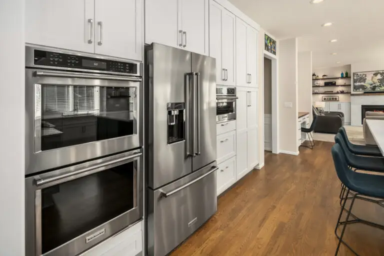 Kitchen appliance wall with wall ovens and refrigerator, open to a bright family room beyond