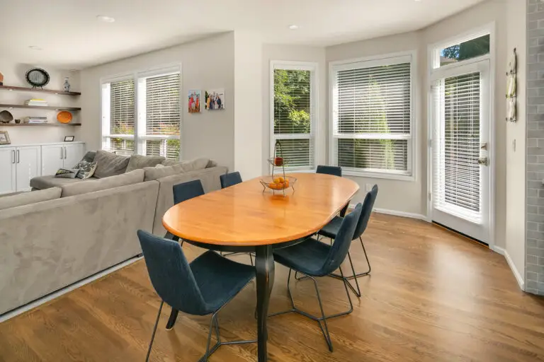 Dining nook with oval wood table, navy chairs, and gray sectional beside windows and a glass patio door