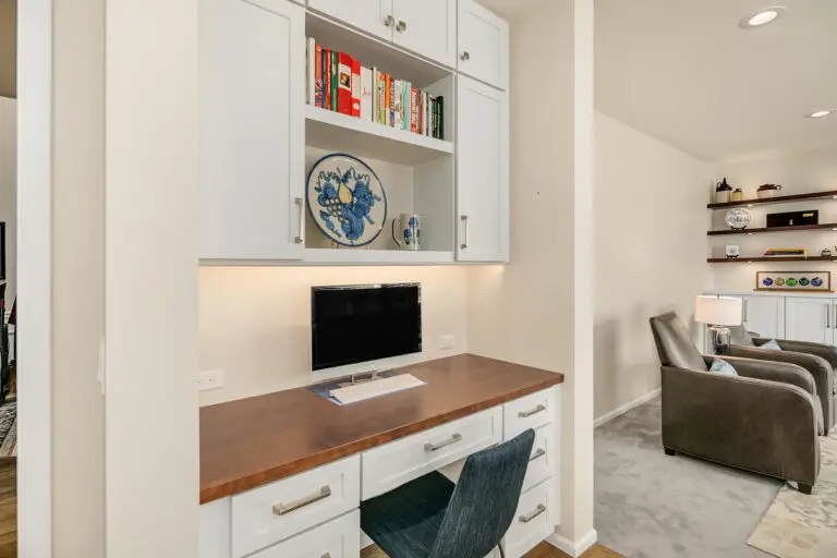 Built-in kitchen desk nook with wood countertop, white cabinets, and shelves holding cookbooks