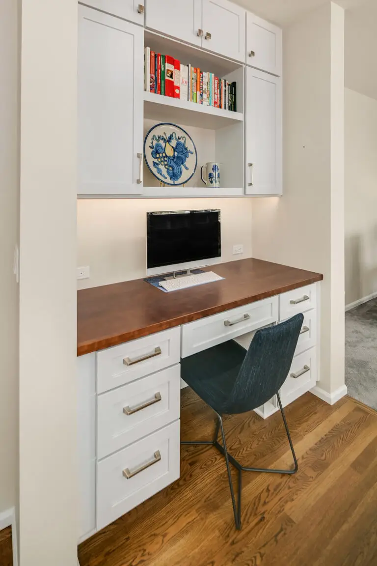 Desk nook with warm wood counter, navy chair, and upper cabinets with cookbook and display shelves