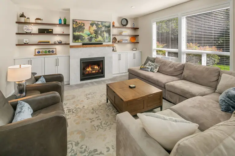 Living area with lit gas fireplace, floating display shelves, and a gray sectional on a patterned rug