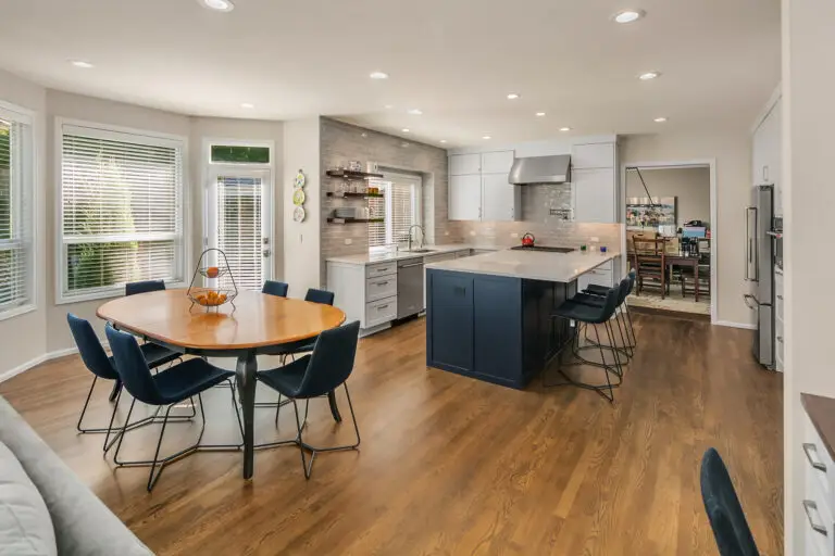 Open kitchen and dining area with navy island, denim bar stools, oval wood table, and oak hardwood floors