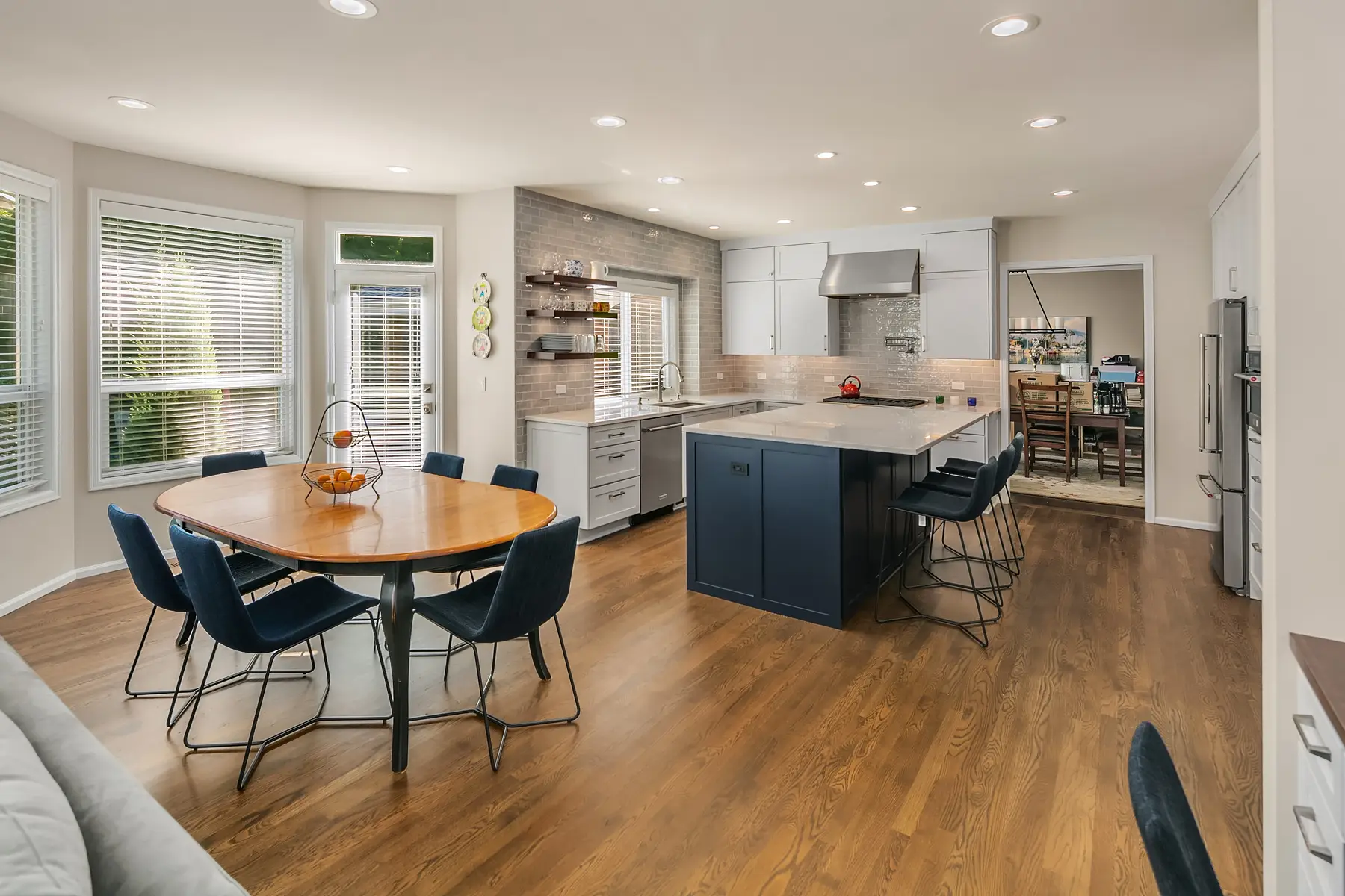 Open kitchen and dining area with navy island, denim bar stools, oval wood table, and oak hardwood floors