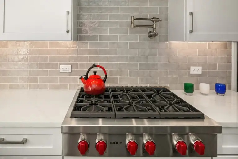 Six-burner Wolf rangetop with red tea kettle, pot filler, and colorful votives against gray Cloe subway tile