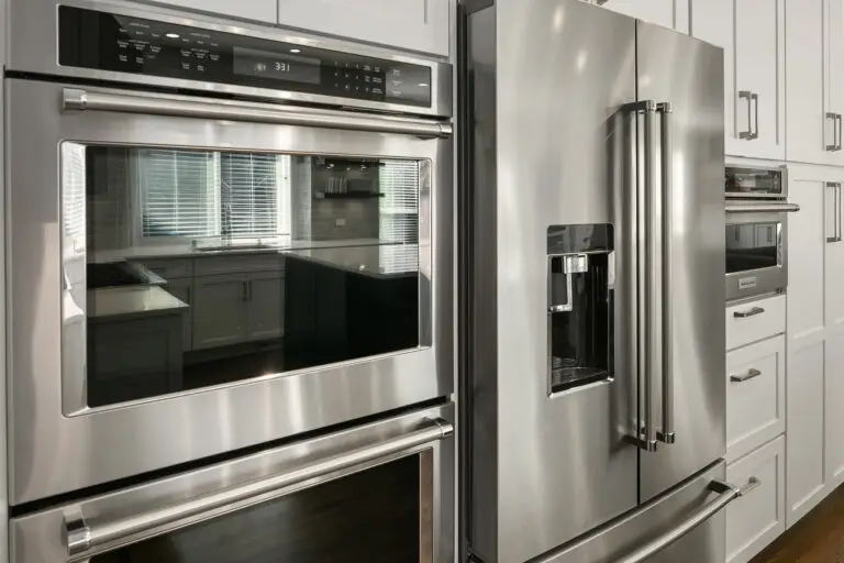 Close view of a stainless double wall oven beside a French-door refrigerator with built-in microwave beyond