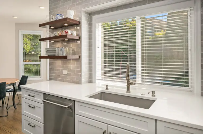 Large single-basin sink under a bright window with brushed nickel faucet, quartz counters, and open shelving