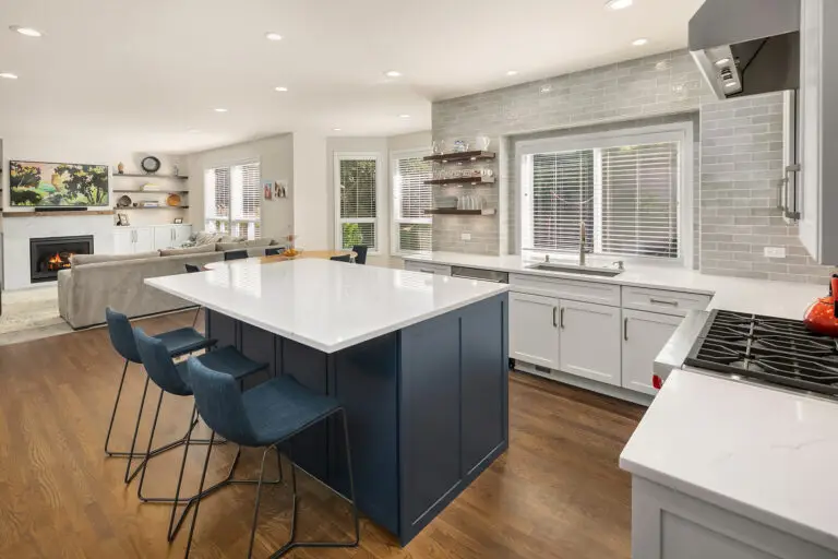 Open-concept kitchen with navy island facing a living room fireplace, white perimeter cabinets and gas rangetop