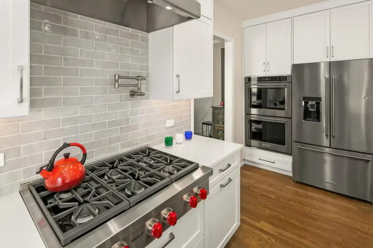 Wolf gas rangetop with red kettle and pot filler against glossy gray Cloe subway tile