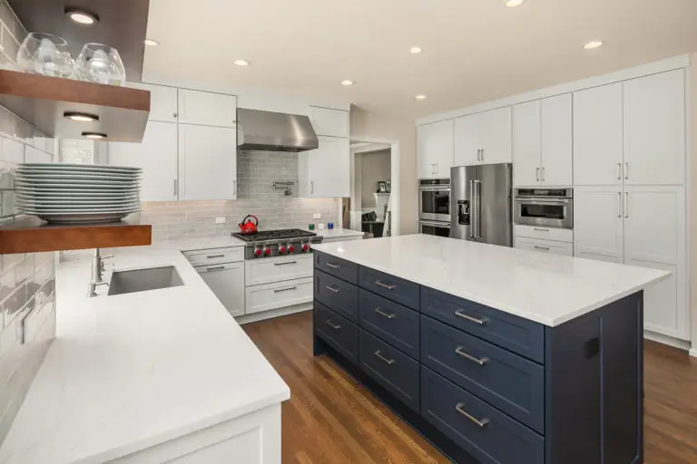 White quartz counters and navy island drawer bank with brushed nickel pulls, stainless appliances beyond