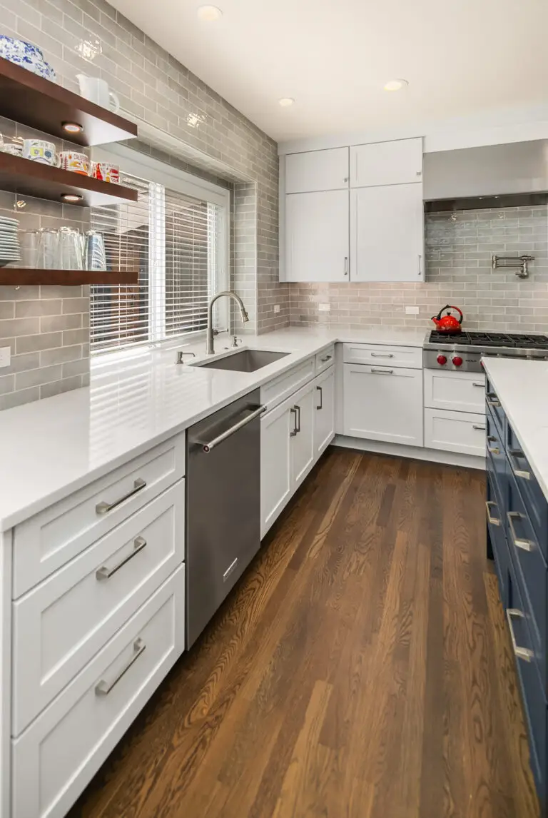 White shaker cabinets and quartz counters along the sink wall, with navy island edge and oak flooring at right