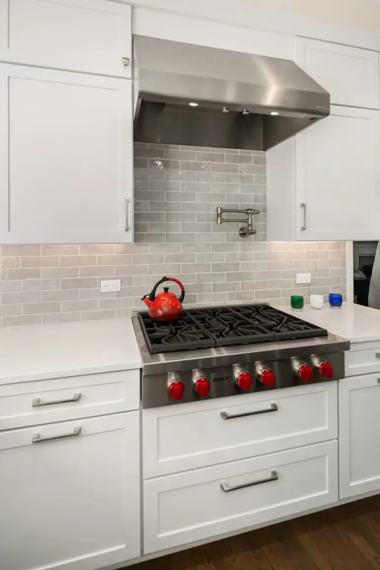 Stainless range hood and pot filler over a six-burner gas rangetop, framed by glossy gray subway tile
