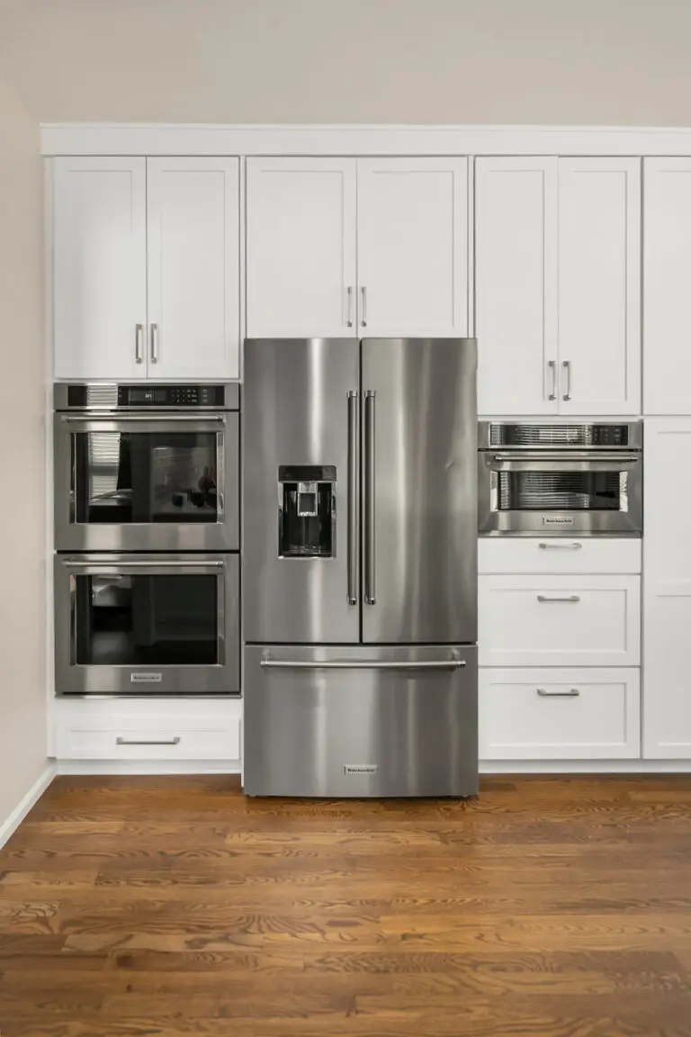 Appliance wall with stainless double wall oven, French-door refrigerator, and microwave set in white cabinetry