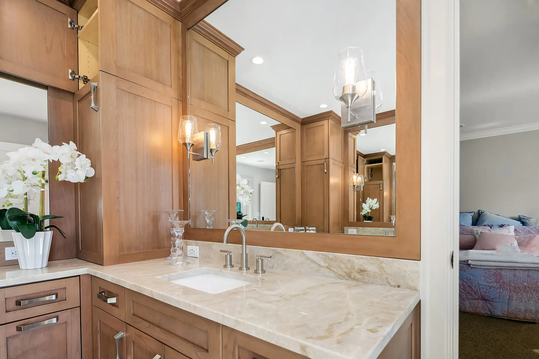 Vanity sink with Taj Mahal quartzite counter and glass sconce, with the bedroom visible through the doorway