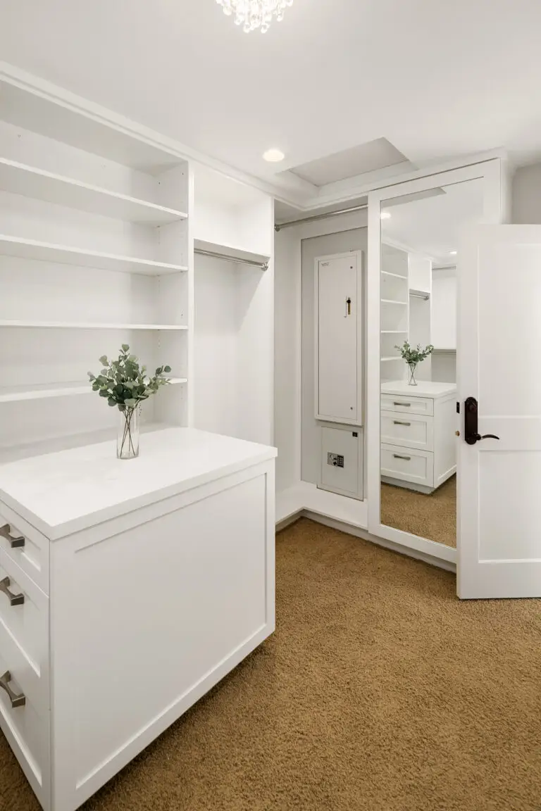 Walk-in closet with mirrored wardrobe, recessed wall safe and white storage island