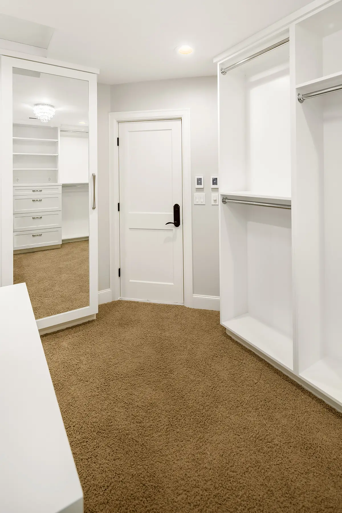 Walk-in closet entry with full-length mirror, white door and open hanging storage