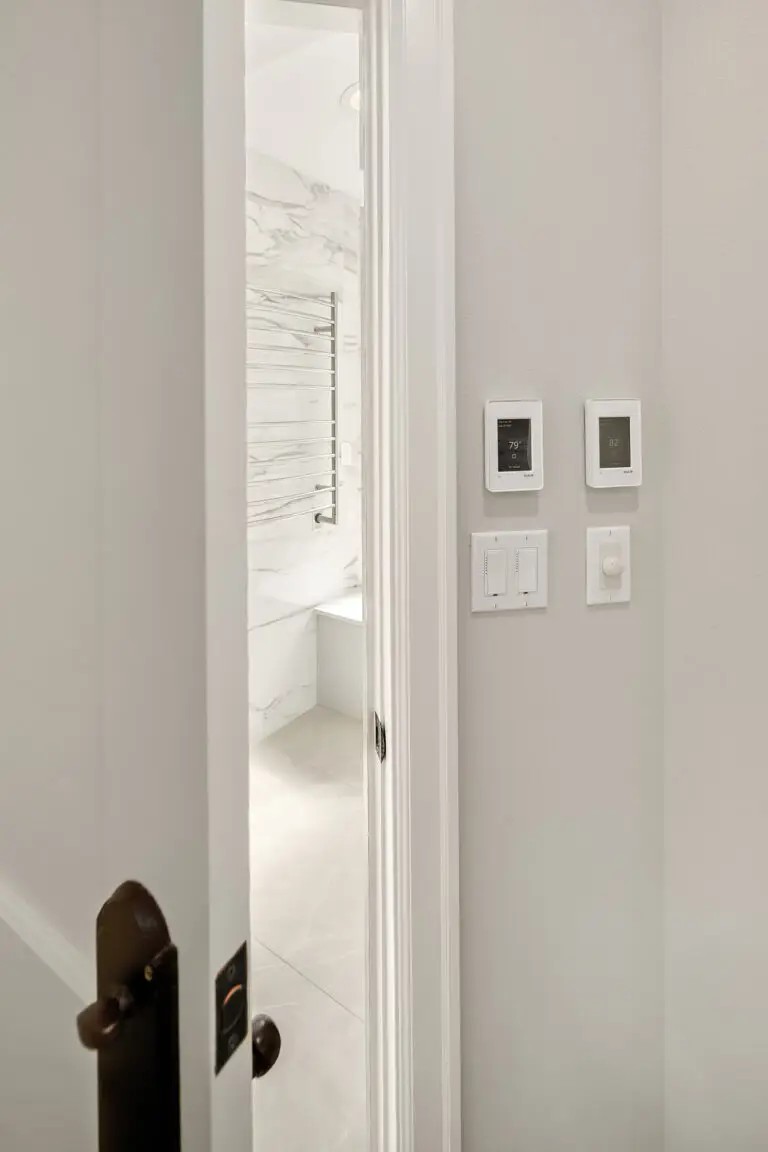 Smart thermostat and towel warmer controls beside the bathroom door with marble-look walls beyond