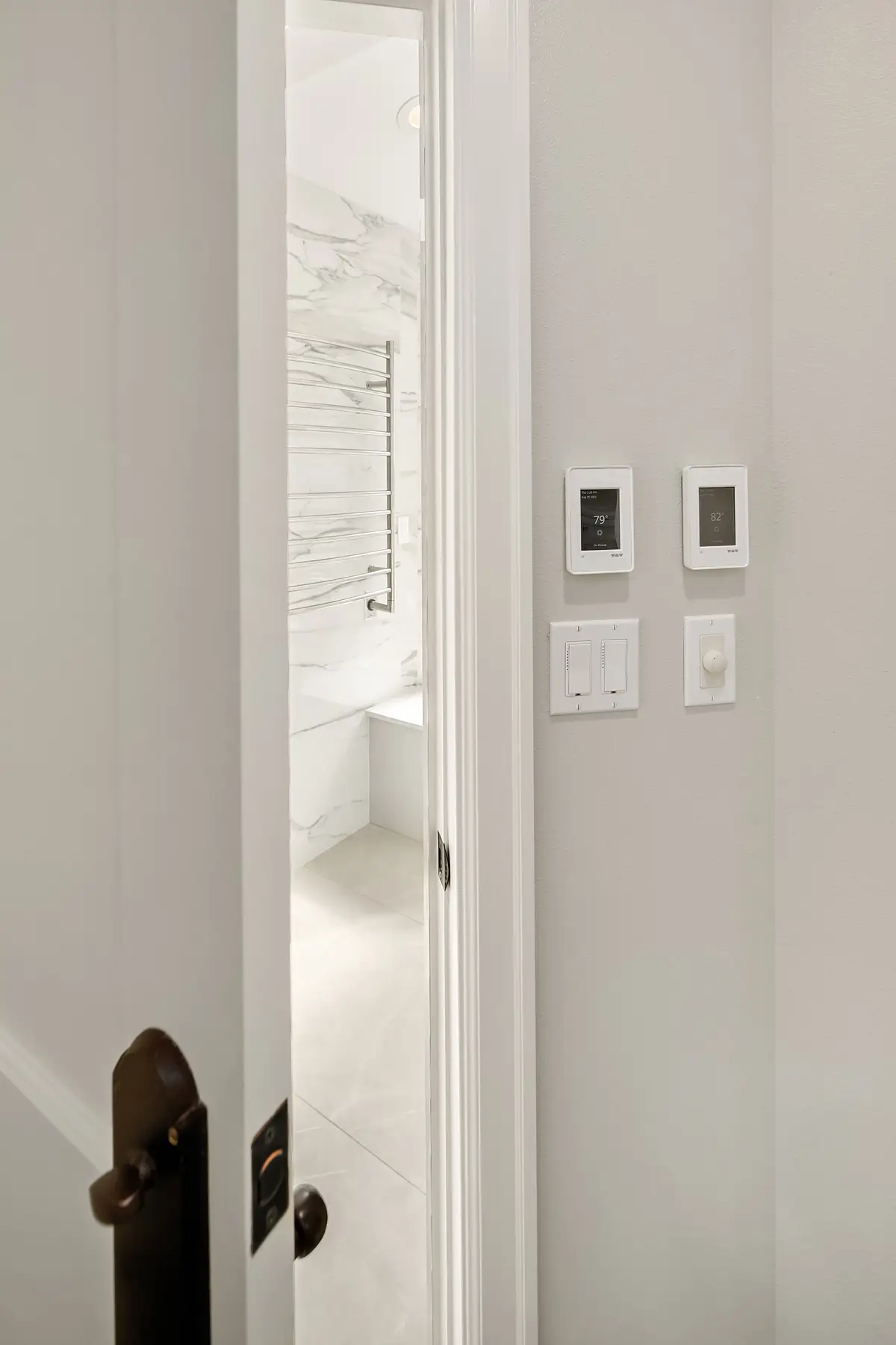Smart thermostat and towel warmer controls beside the bathroom door with marble-look walls beyond