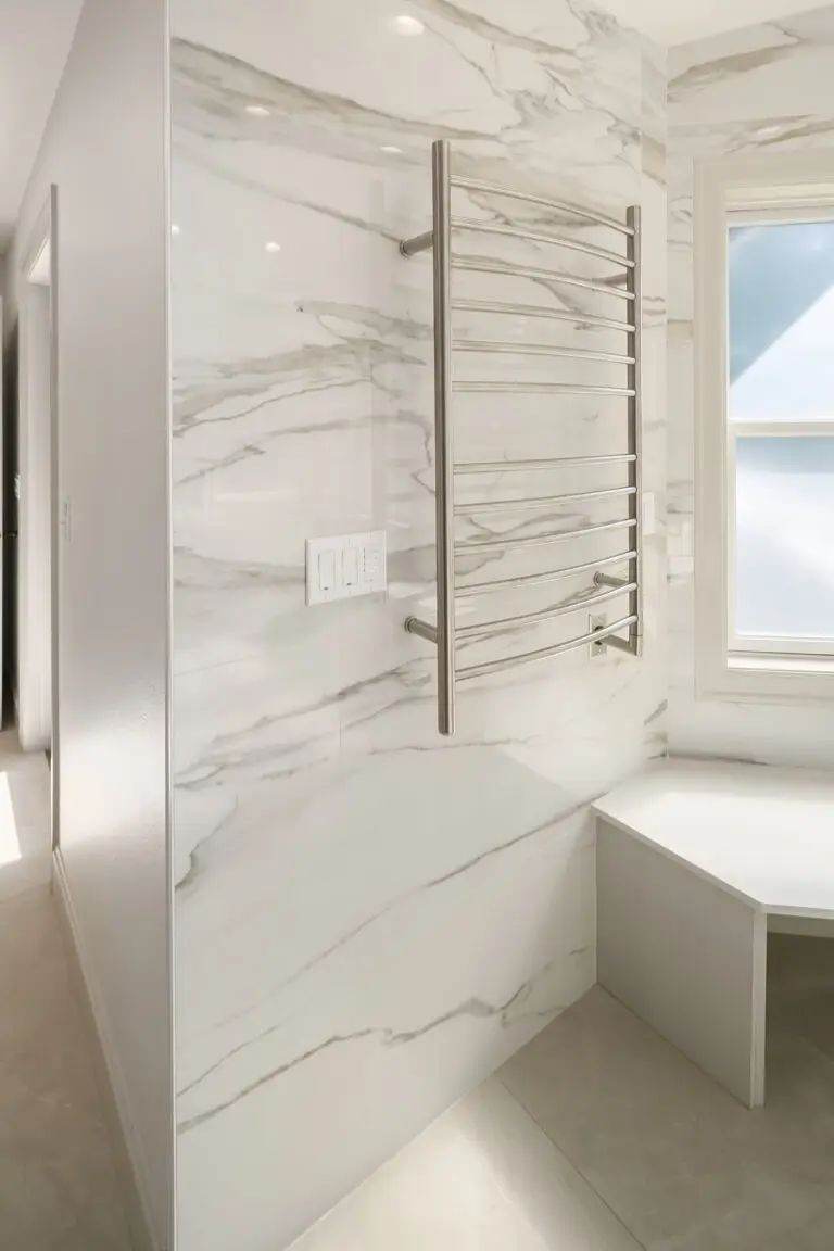 Heated towel warmer on veined slab wall beside a window bench in the remodeled bathroom