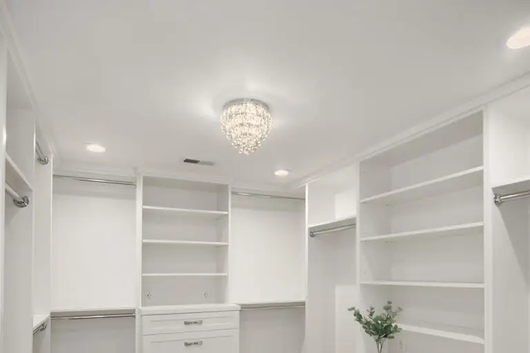 Crystal chandelier and recessed lighting above white built-in shelving in the walk-in closet
