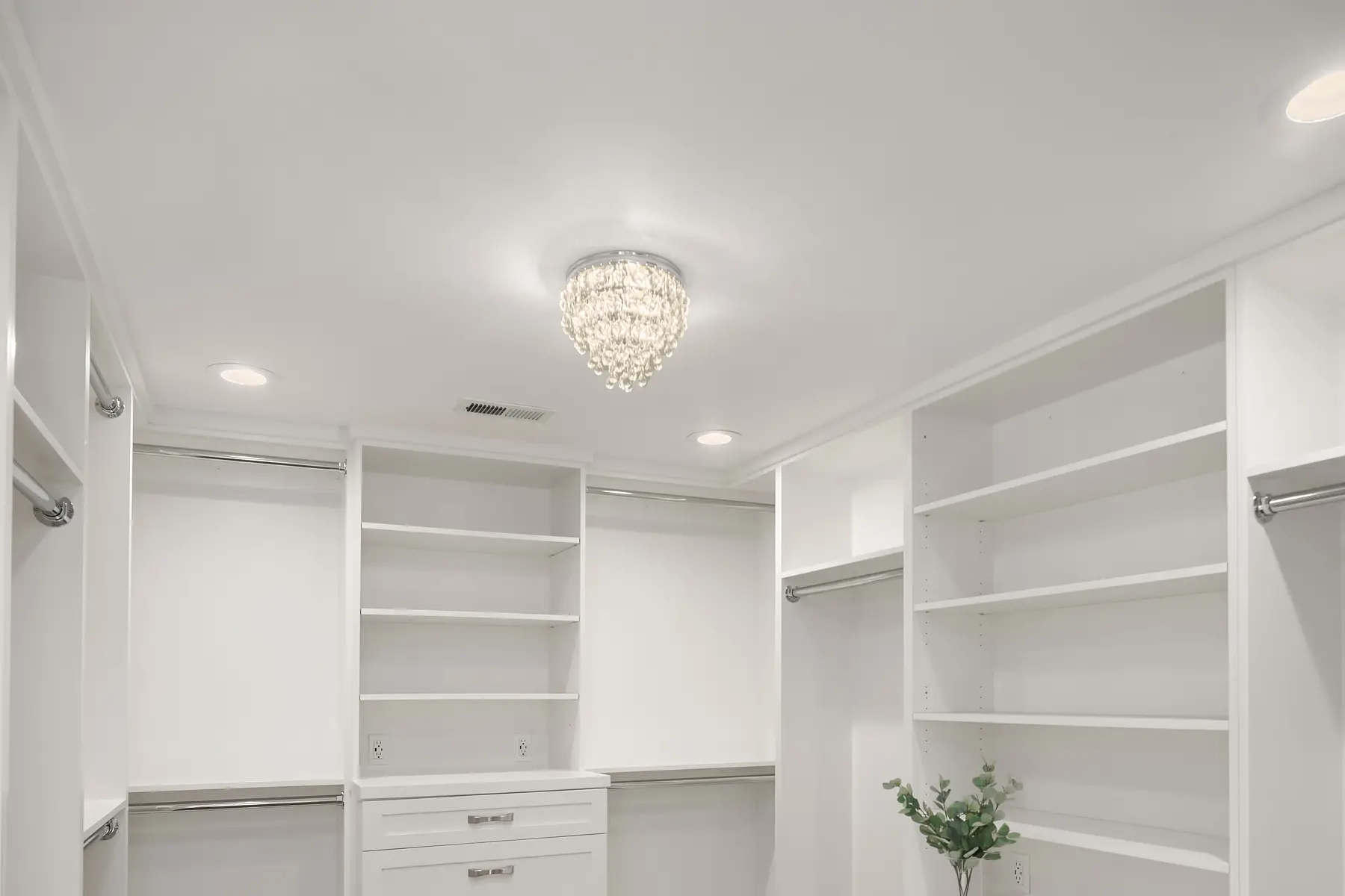 Crystal chandelier and recessed lighting above white built-in shelving in the walk-in closet