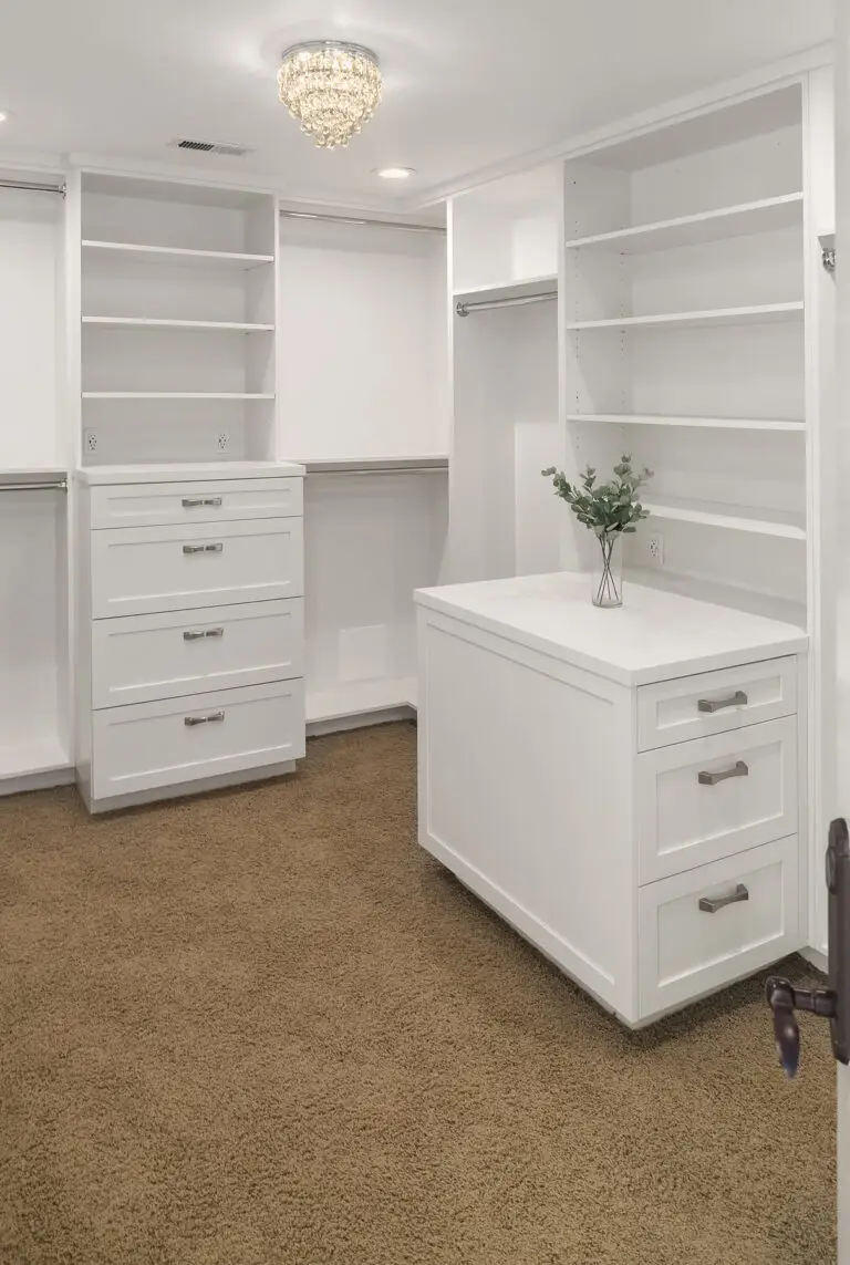 Walk-in closet with crystal chandelier, white dresser island and plush carpet