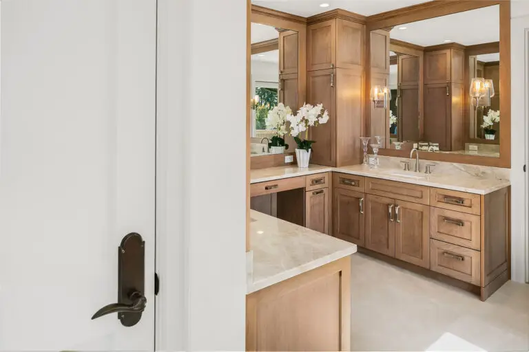 Wood-framed mirrors and cherry vanity with Taj Mahal quartzite counters seen through the bathroom doorway