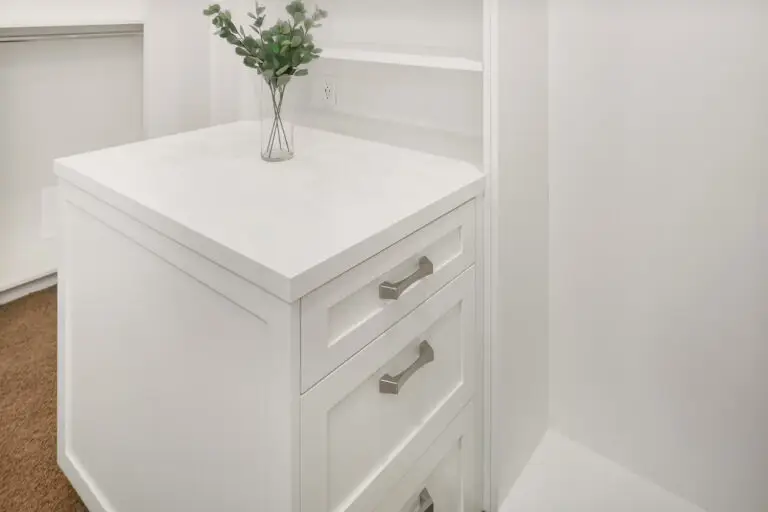 White closet island dresser topped with a glass vase of eucalyptus stems