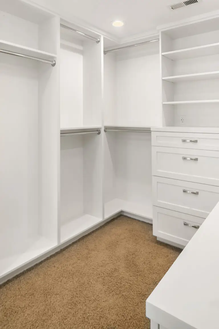 Corner of walk-in closet with double hanging rods, built-in drawers and white countertop