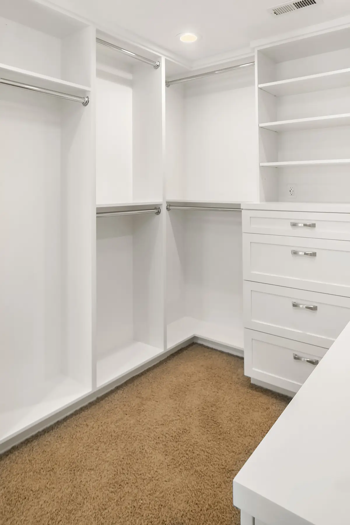 Corner of walk-in closet with double hanging rods, built-in drawers and white countertop