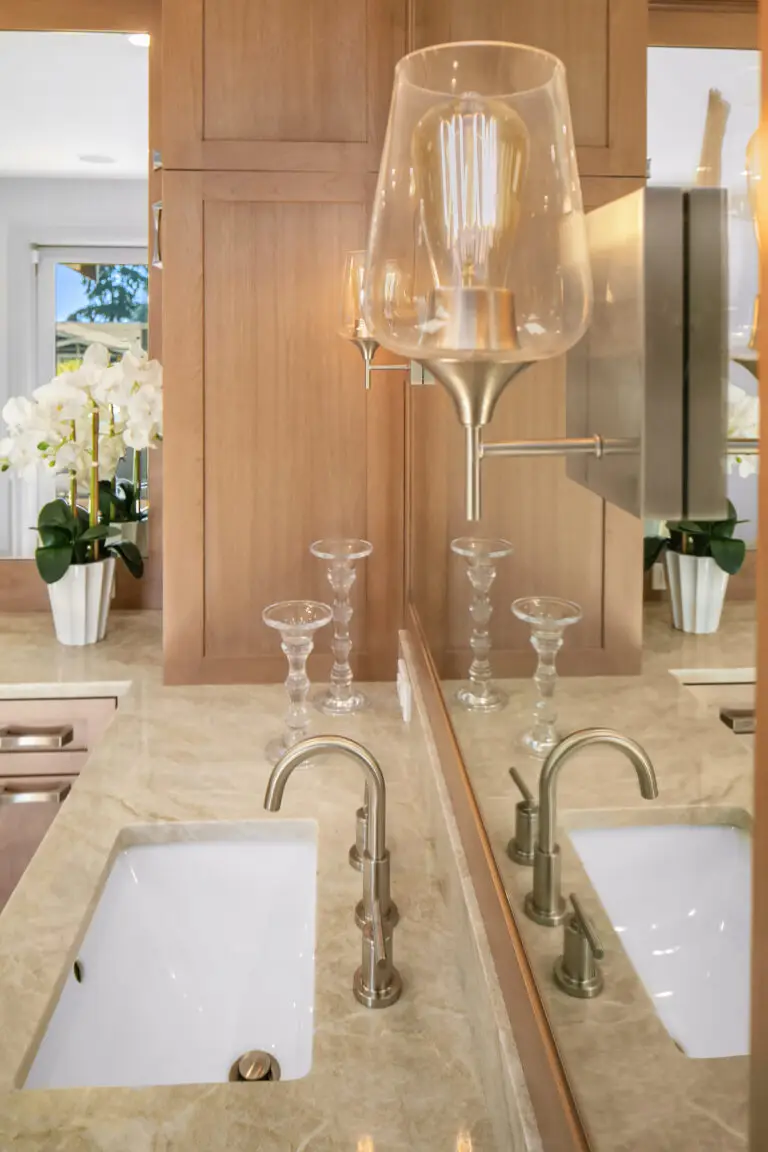 Brushed nickel faucet and sconce at a Taj Mahal quartzite vanity with glass candlesticks and orchids