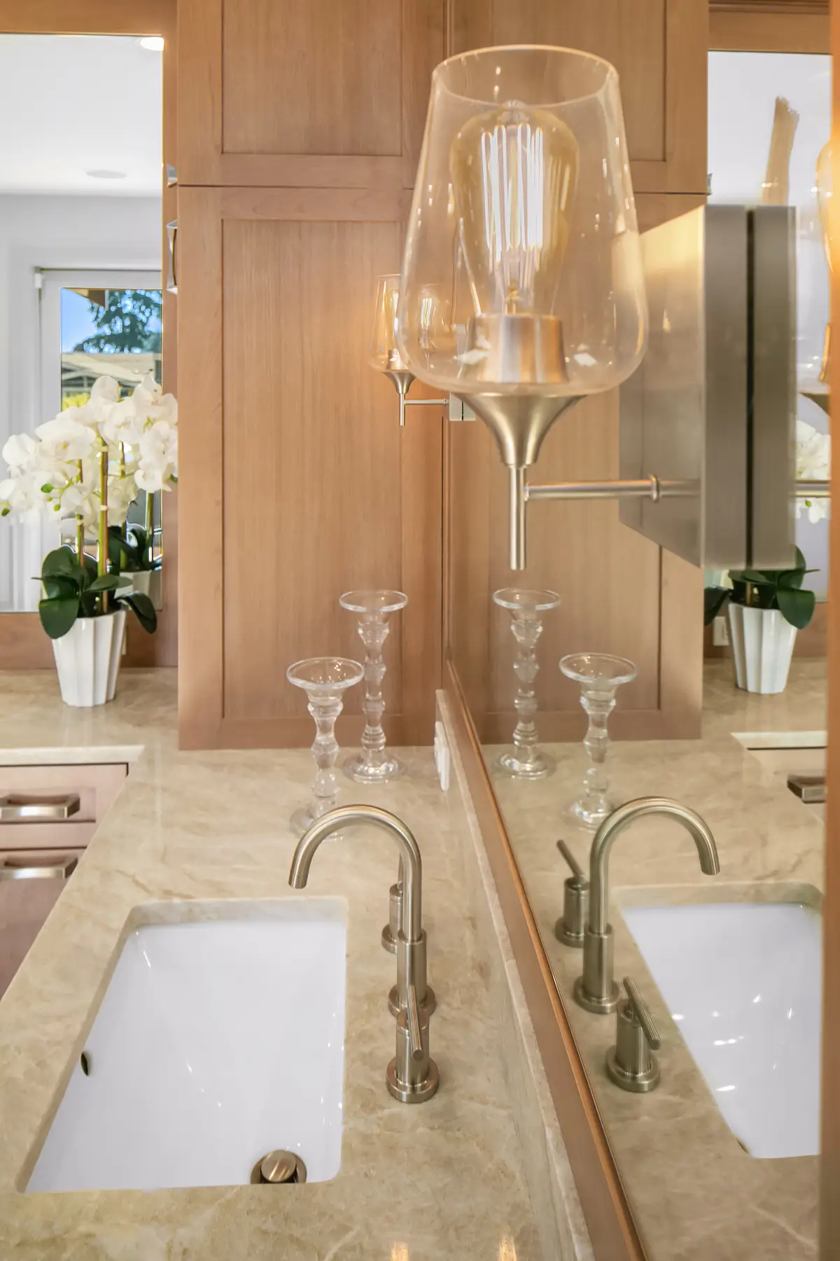 Brushed nickel faucet and sconce at a Taj Mahal quartzite vanity with glass candlesticks and orchids