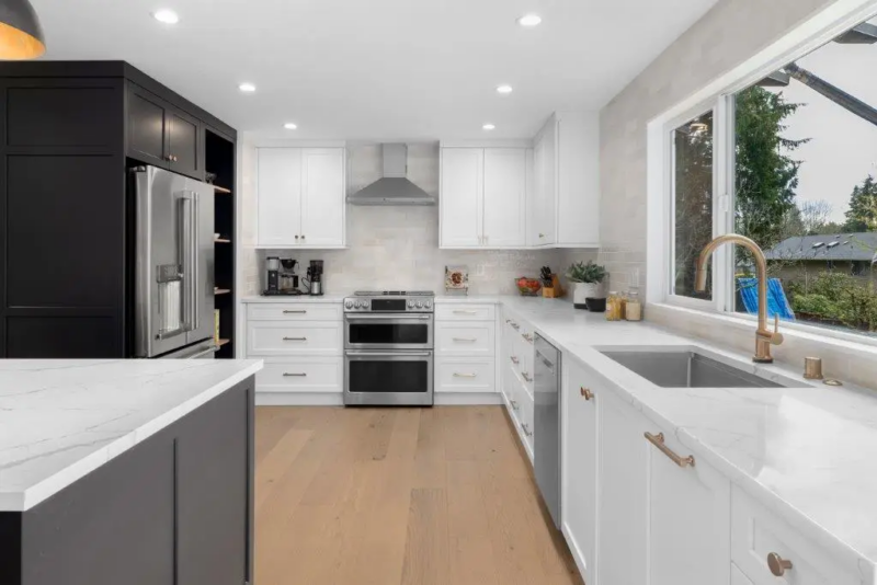 Kitchen with black pantry cabinets, stainless fridge, white quartz counters, brass faucet and wide picture window