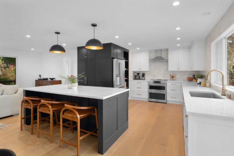 Black kitchen island with marble-look quartz top, wood bar stools, black dome pendants and white perimeter cabinets