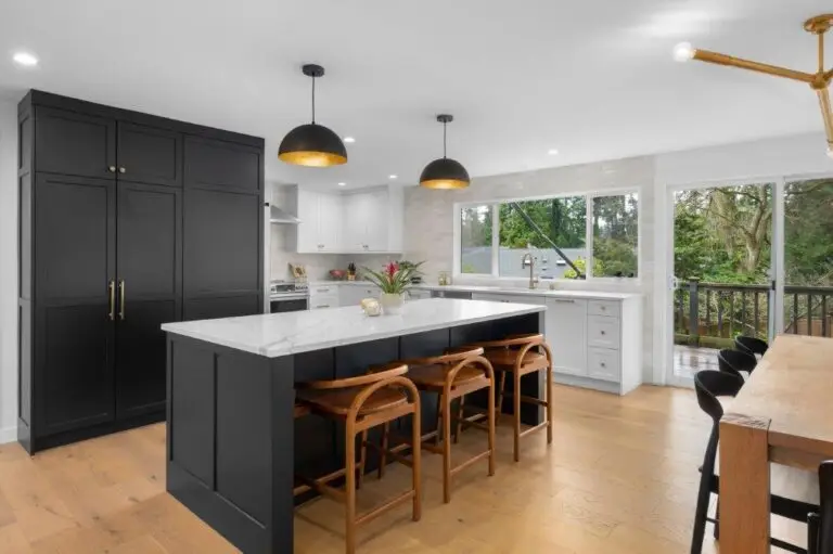 Black cabinet wall and island with marble-look quartz top, wood stools and gold-lined dome pendants by sliding doors
