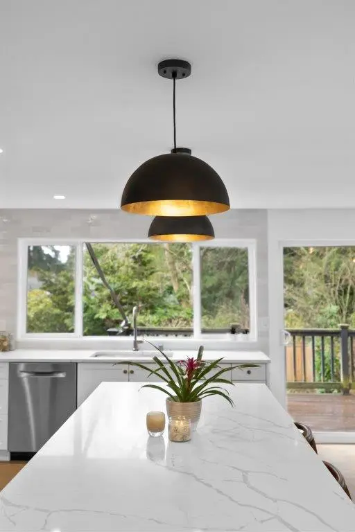 Black dome pendants with gold interiors over a marble-look quartz island with potted bromeliad and garden view