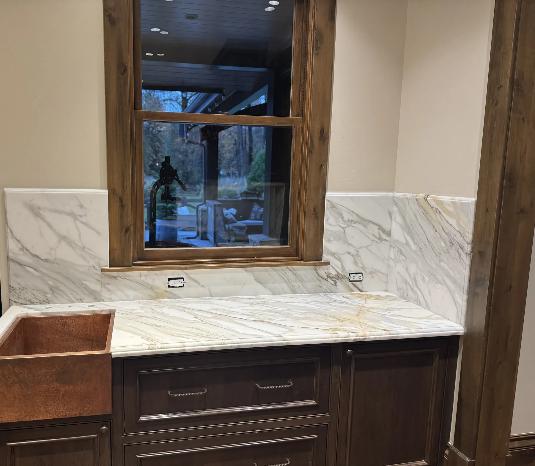 Calacatta Gold marble backsplash panels flanking a window above a copper farmhouse sink