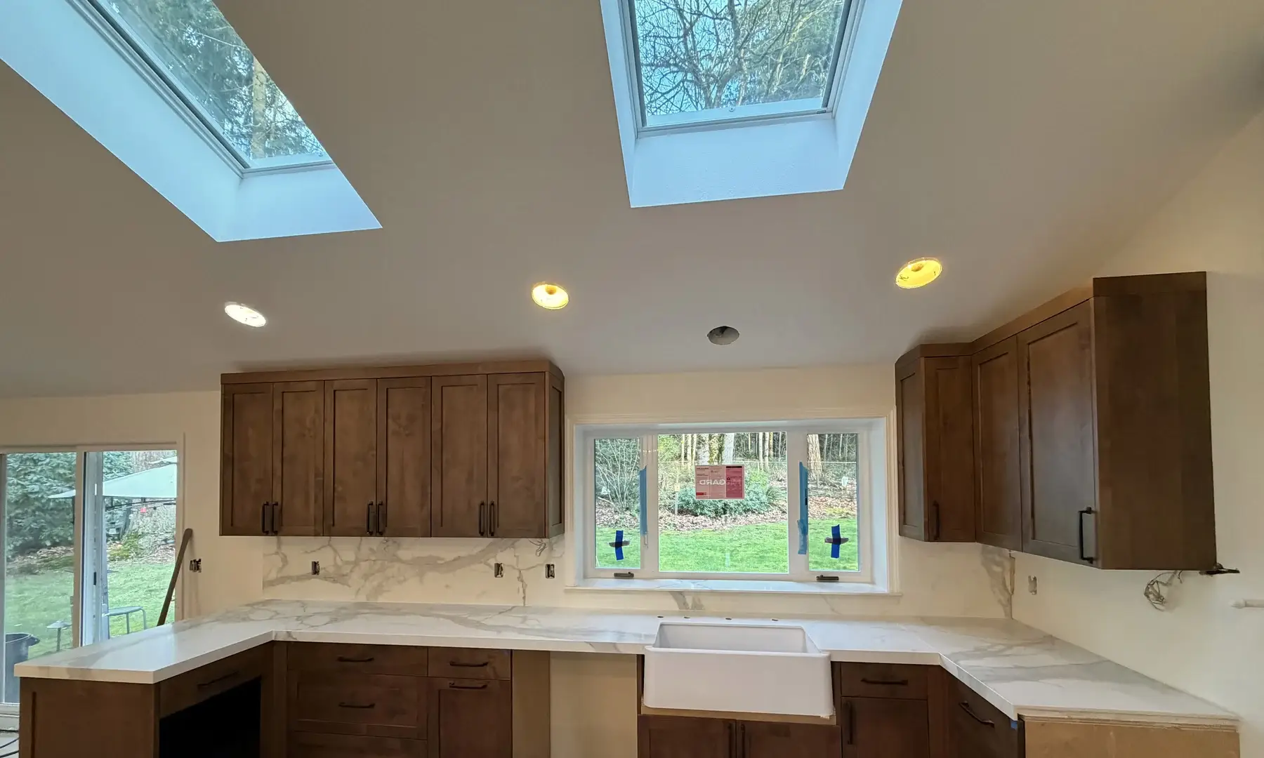 U-shaped kitchen with white Calacatta porcelain countertops, full-height backsplash, and skylights above.