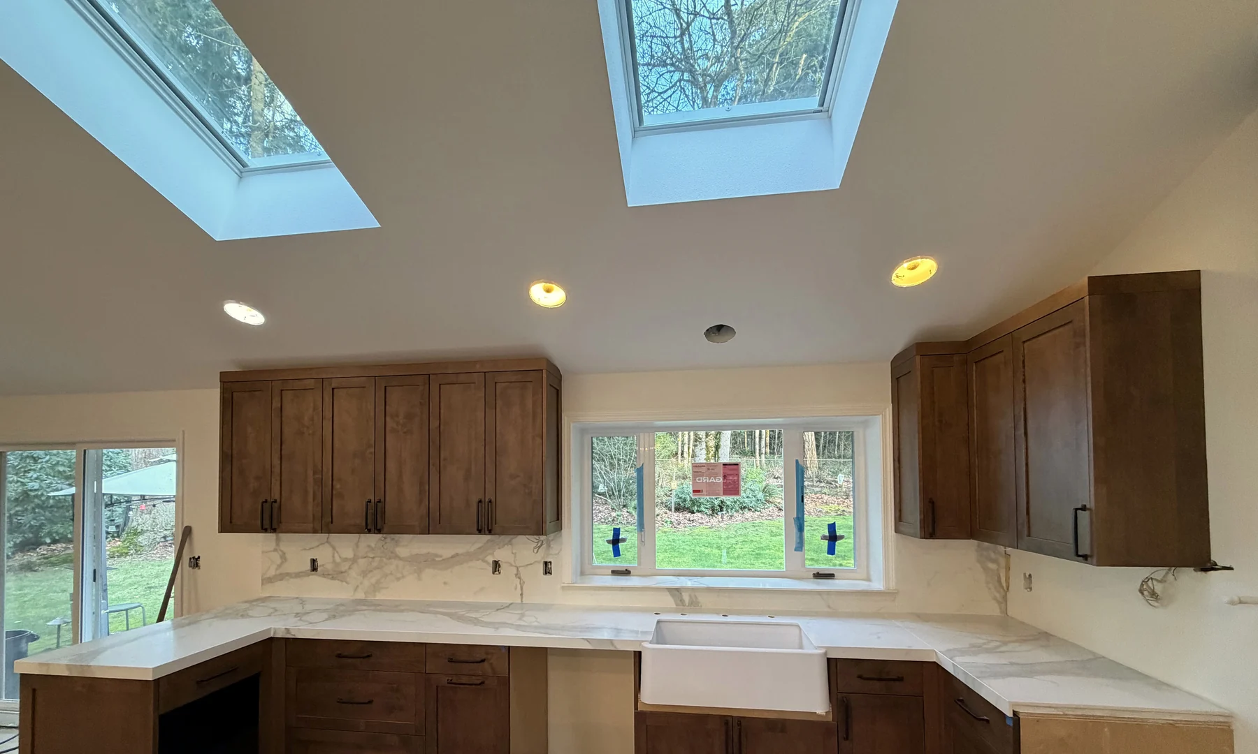 U-shaped kitchen with white Calacatta porcelain countertops, full-height backsplash, and skylights above.