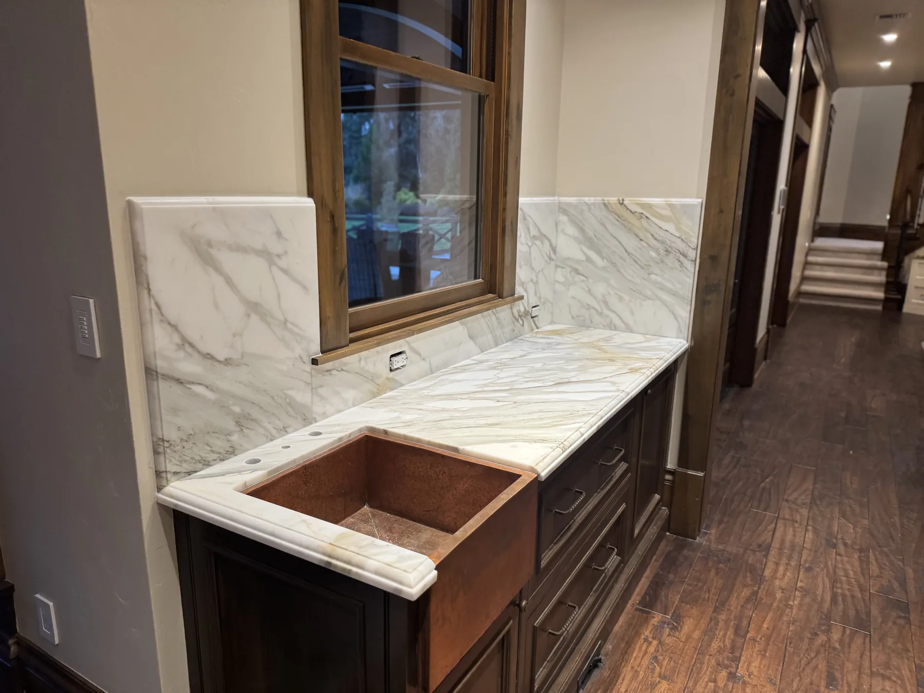 Copper farmhouse sink set into a Calacatta Gold marble bar counter with a matching marble backsplash