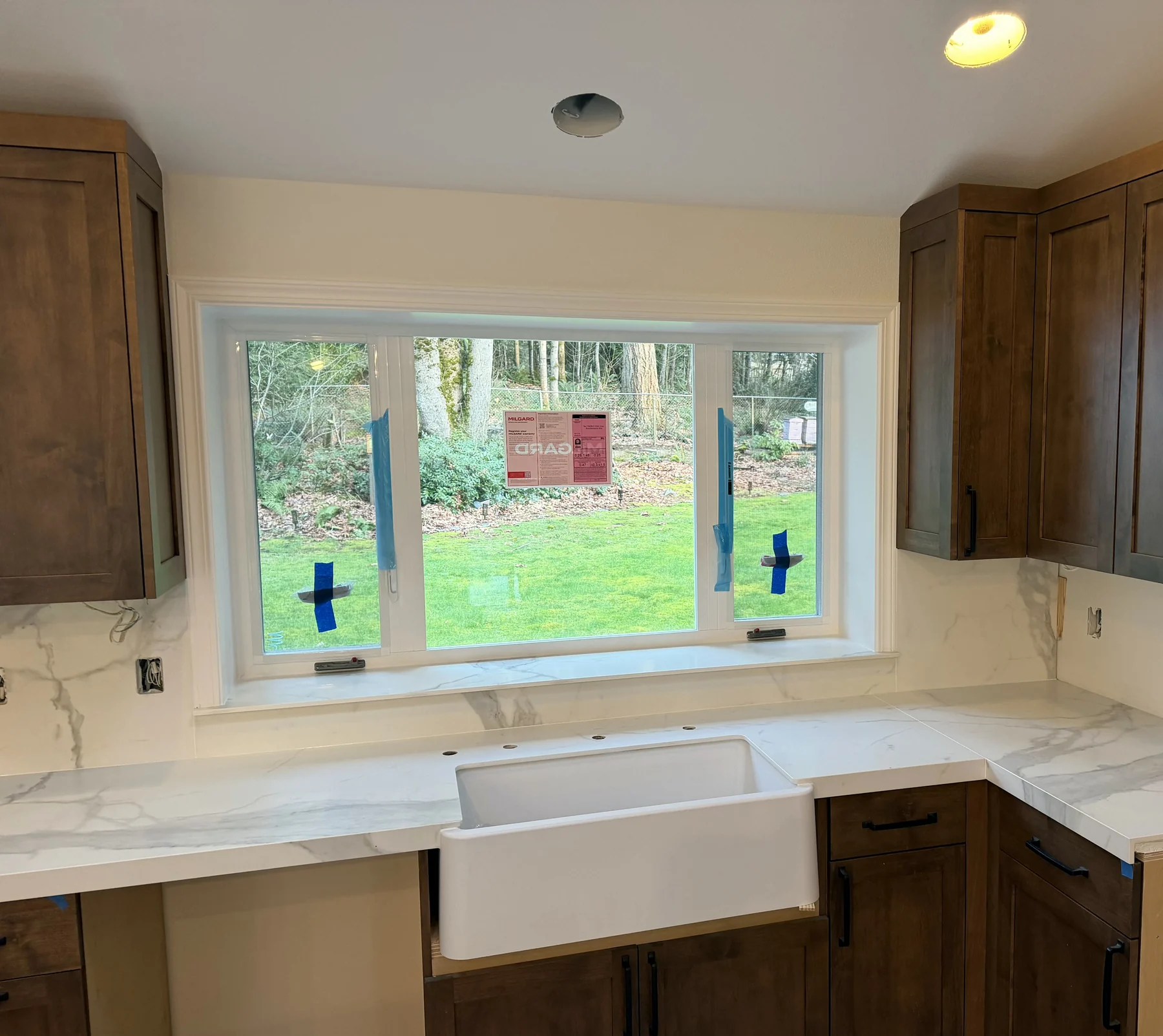 Farmhouse apron sink beneath a window with porcelain countertops and full-height backsplash wrapping the window return.