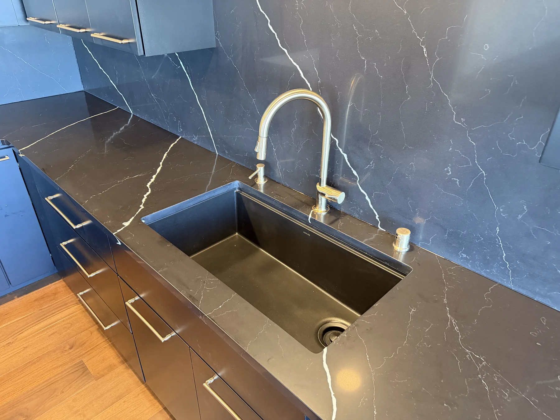 Matte black undermount sink and brushed bronze faucet set into a black quartz countertop with white veining